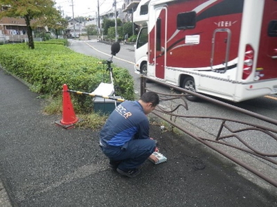 車道近くで人が機材を用いて測定する様子